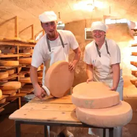 Ein Mann und eine Frau stehen im Käsekeller und bürsten Käselaibe