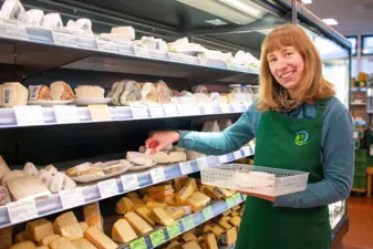 Mitarbeiterin im Biomarkt legt Käse in ein Regal und blickt in die Kamera