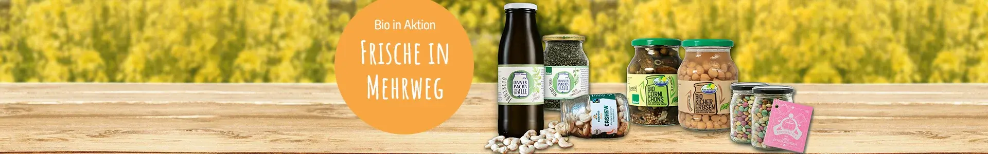 Verschiedene Produkte in Mehrweg-Glas auf einem Brett, im Hintergrund blühender Raps. Ein oranger Kreis mit Schrift: Bio in Aktion. Frische in Mehrweg