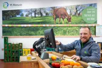 Kassierer sitzt an der Kasse, im Vordergrund Produkte auf dem Kassenband