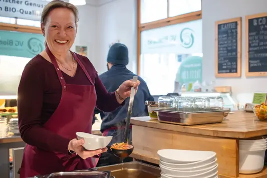 Mitarbeiterin im Biobistro füllt Suppe in eine Schüssel