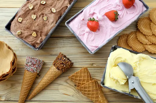 Schokoladeneis, Vanilleeis und Erdbeereis in rechteckigen Formen, daneben Eiswaffeln. Bild: AdobeStock_denio109