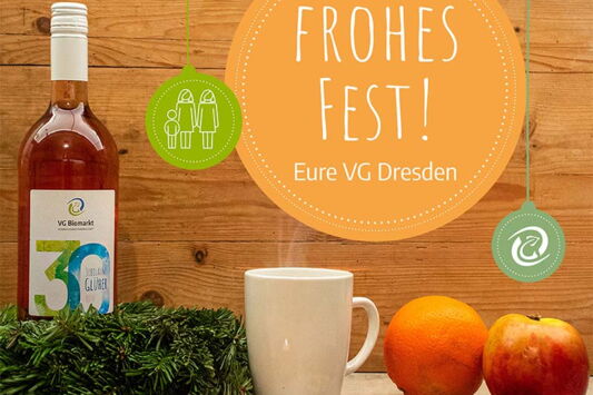 VG-Glühwein mit Weihnachtskranz und Keksen. Vor einem Holzhintergrund das Logo der VG und der Text "Frohes Fest - Eure VG Dresden"