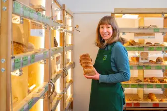 Mitarbeiterin im Markt steht vor einem Brotregal und hält ein Brot in der Hand