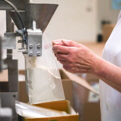 Mitarbeiterin der Rolle Mühle füllt Mehl in eine Verpackung