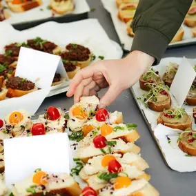 Snacks und Schnittchen auf drei Tabletts, eine Hand greift nach einem der Schnittchen.