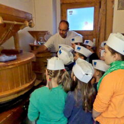 Bäcker zeigt einer Gruppe Kinder die Getreidemühle