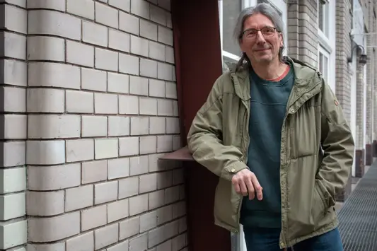 Ralf Werner lehnt vor dem Eingang eines Hauses und lacht in die Kamera