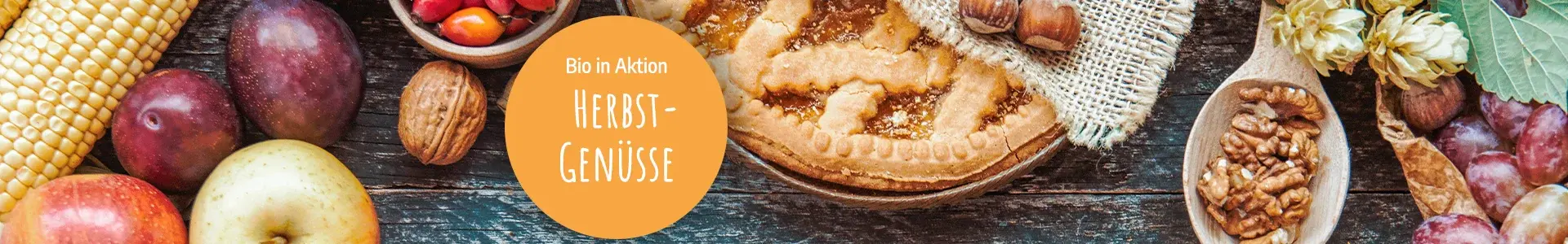 Herbstliche Gemüse und Obst, ein Kuchen auf Holzuntergrund. Text "Bio in Aktion: Herbstgenüsse" auf orangem Kreis. Hintergrundbild: AdobeStock_RomanWhale studio