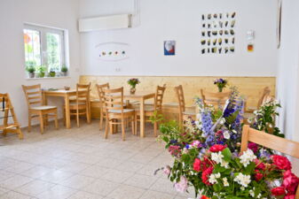 Mehrere Tische und Stühle im Sitzbereich des Bistros, im Vordergrund ein Blumenstrauß