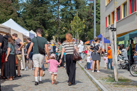 Eine Familie mit Kind schlendert über ein Festgelände mit vielen Menschen