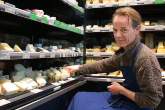 Mitarbeiter im Biomarkt legt Käse in ein Käseregal