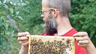 Imker der Imkerei Heinrichsgarten hält Honigwabe mit Bienen