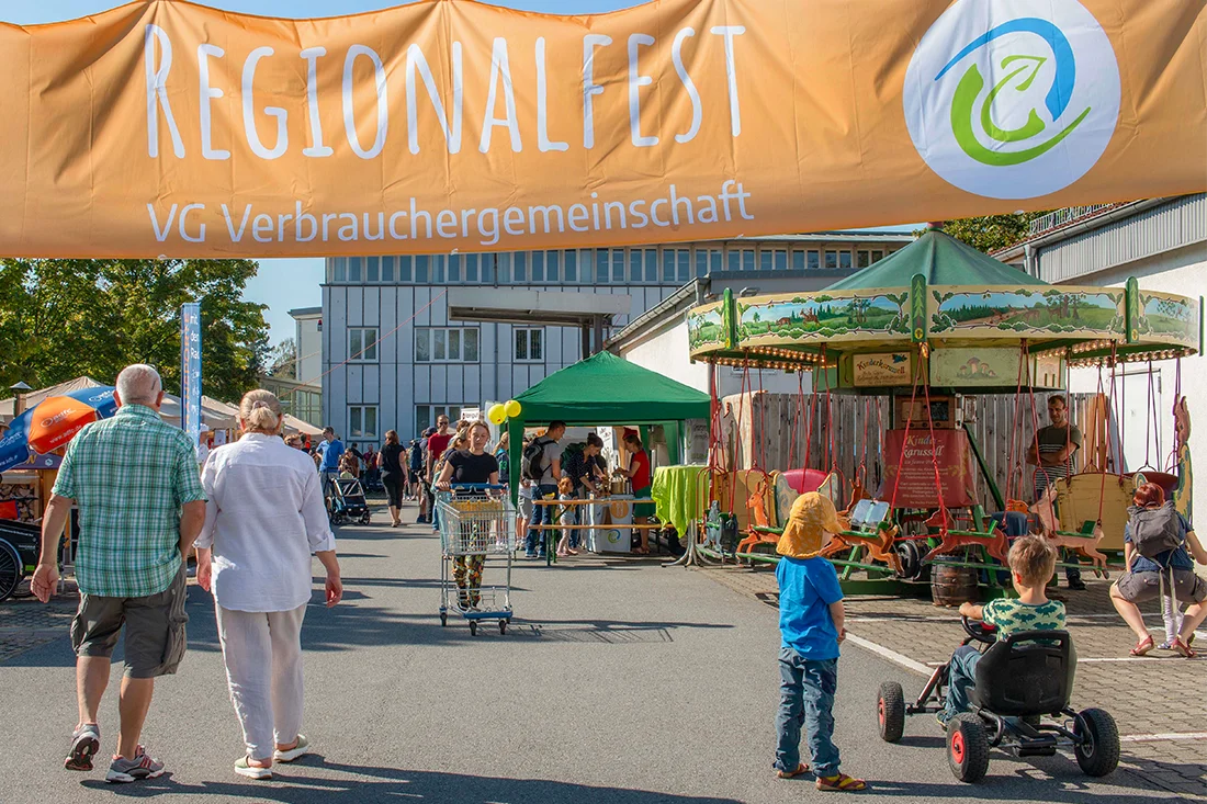Menschen besuchen das Regionalfest der VG 2023, im Hintergrund das Festgelände bei Sonnenschein
