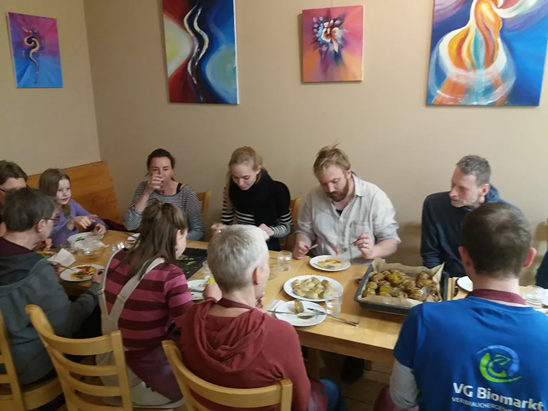 Menschen sitzen um einen Tisch und essen Kartoffelgerichte