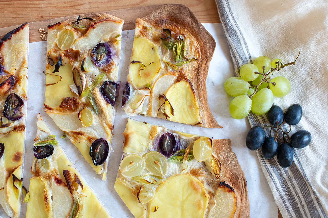 Flammkuchen mit Kartoffeln, Lauch und Trauben in Stücke geschnitten auf Papier