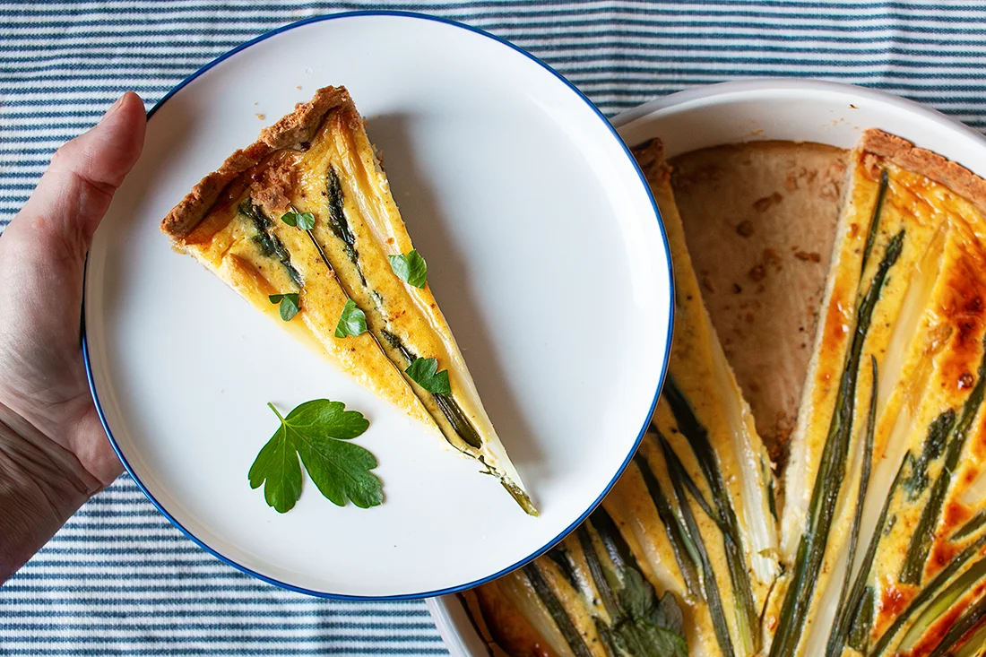 Hand hält einen Teller mit einem Stück Spargelquiche mit weißem und grünem Spargel