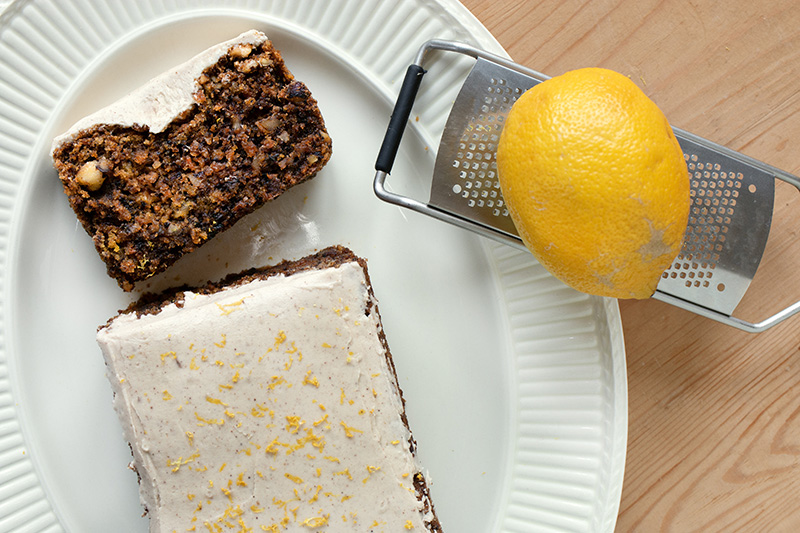 Karottenkuchen mit Zimt-Frosting auf einem Teller, daneben eine Zitrone auf einer Reibe