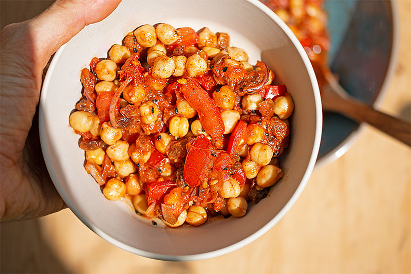 Hand hält Kichererbsen-Salat mit Tomaten in einer kleinen Schüssel