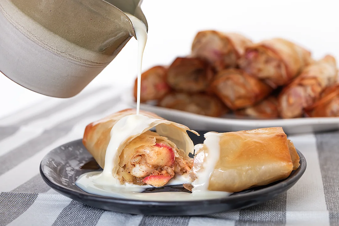 Vanillesauce wird über Apfelstrudel auf einem Teller gegossen