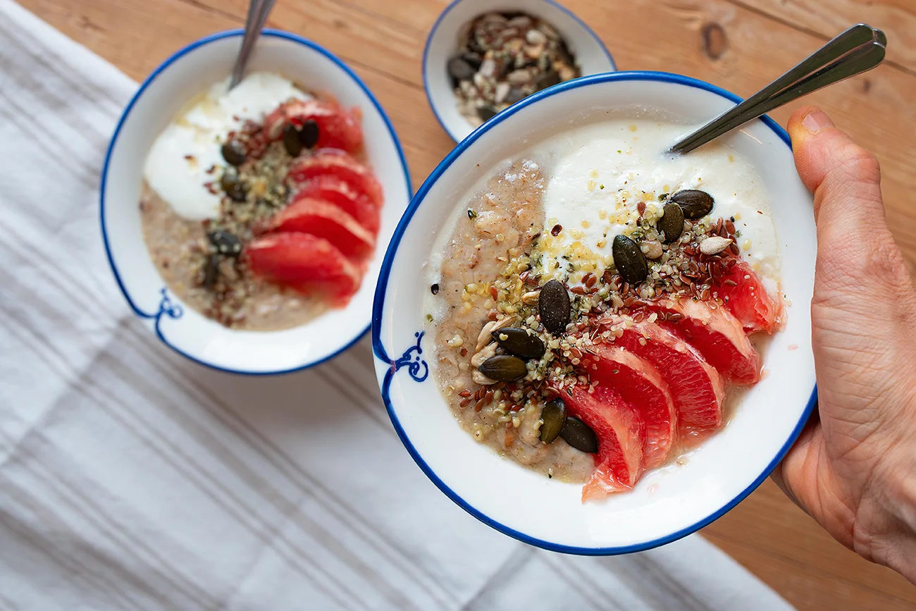 Hand hält eine Schüssel Haferporridge mit Grapefuit, Saaten und Kardamom