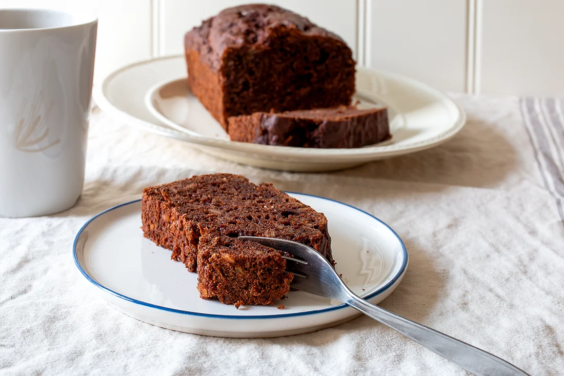 Schokoladen-Zucchini-Kuchen auf einem Teller und einer Kuchenplatte im Hintergrund