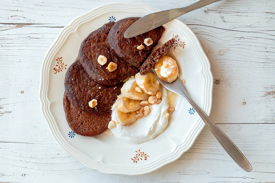 Schoko-Pancakes mit Bananenscheiben und veganer Frischcreme auf einem Teller