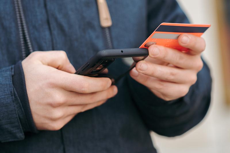 Person in blauer Jacke hält Mobiltelefon und Kreditkarte in der Hand