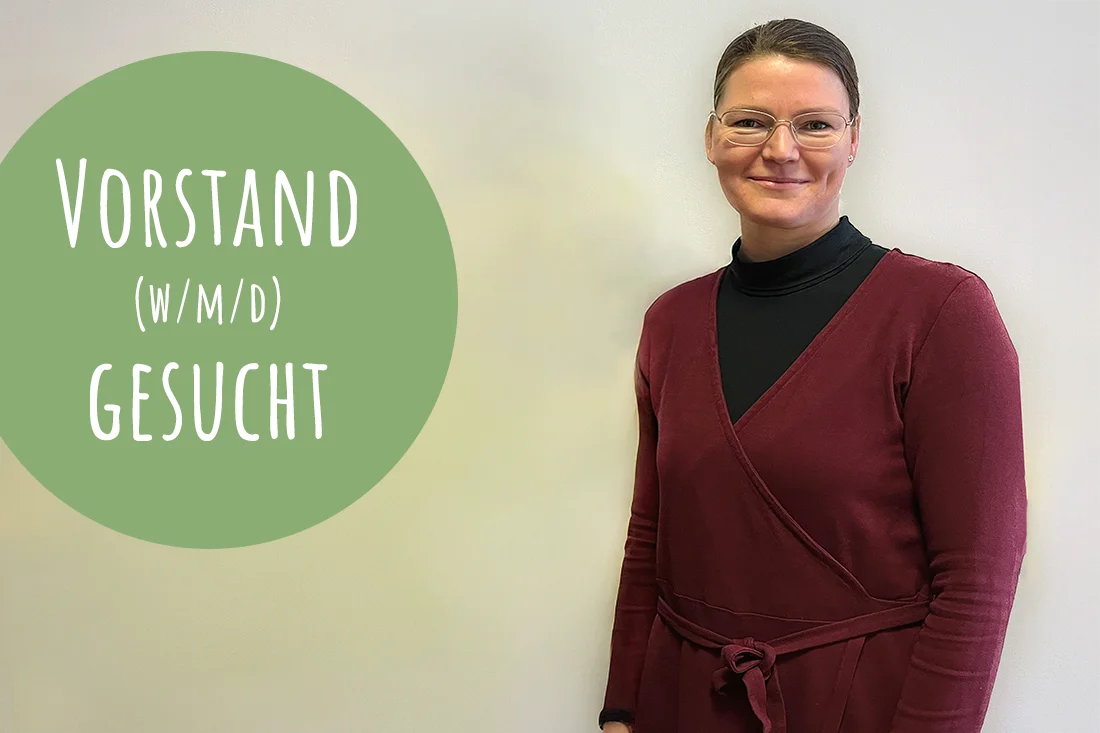 Frau steht vor einer weißen Wand und blickt in die Kamera. Ein grüner Kreis mit weißer Schrift: Vorstand (m/w/d) gesucht.