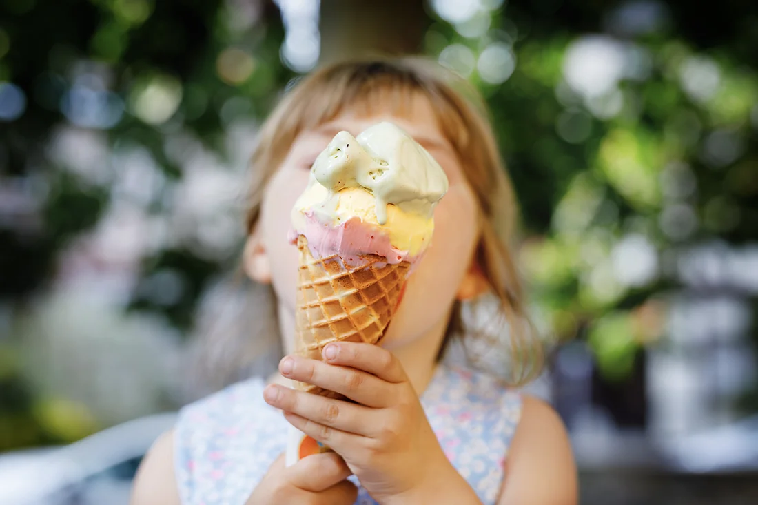 Kind hält eine Eistüte mit drei Eissorten in die Kamera. Bild: AdobeStock_ Irina Schmidt