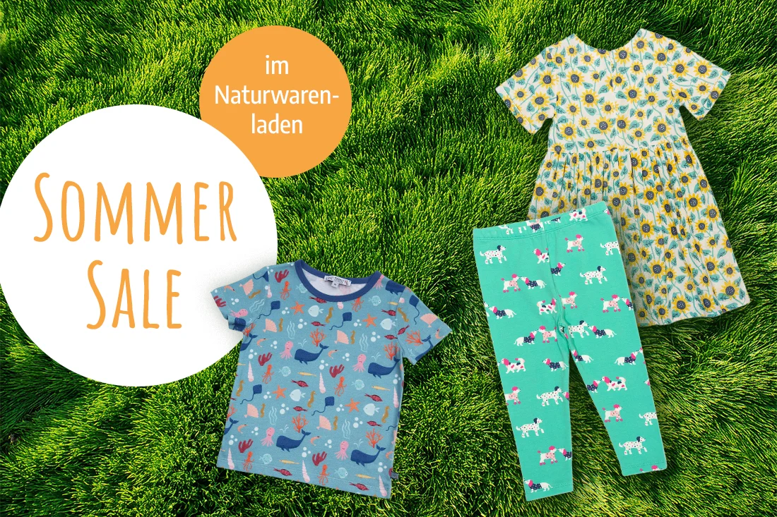 Bunte, sommerliche Kinderkleidung auf einer Wiese. Text auf weissem und orangem Kreis: Sommer Sale im Naturwarenladen.