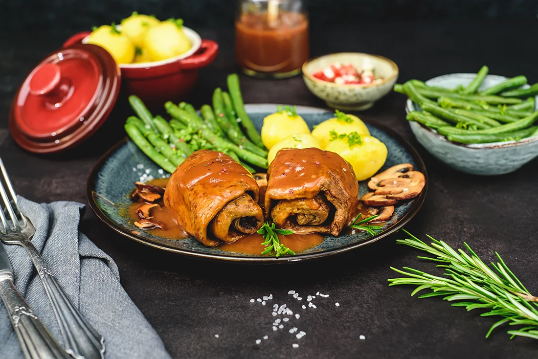 Vegane Seitanroulade festlich zubereitet mit Bohnen, Kartoffeln und Pilzsauce auf einem Teller