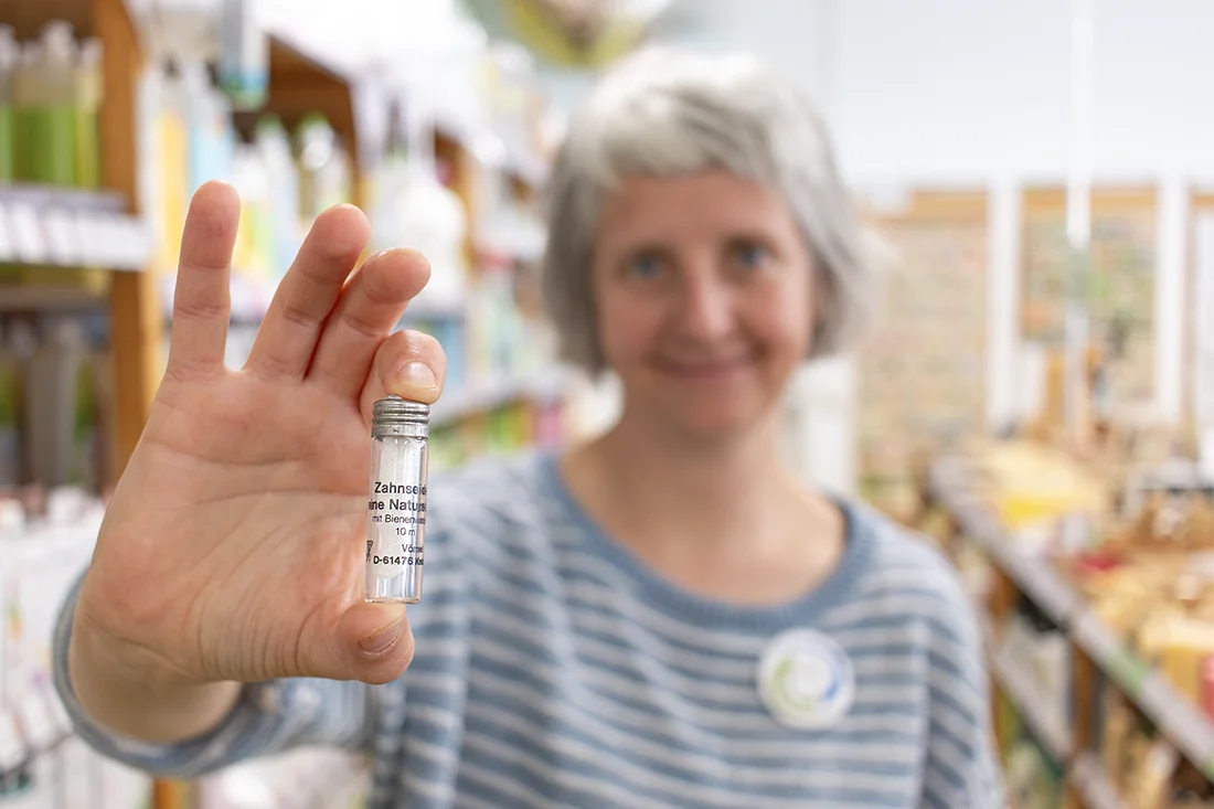 Eine Frau hält Zahnseide in einem Glas-Flakon in die Kamera