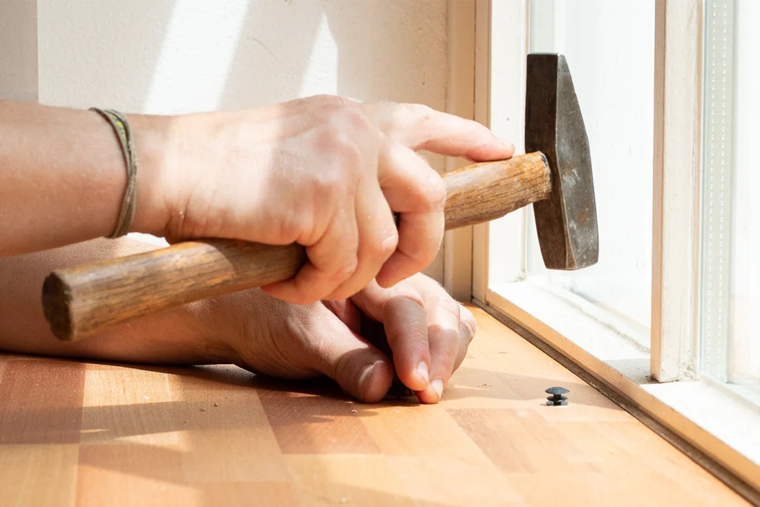 Eine Hand hält einen Hammer und schlägt einen Nagel in ein Brett