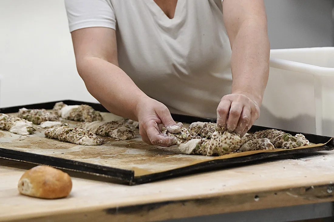 Bäcker formt Dinkelbrötchen mit Saaten auf einem Blech