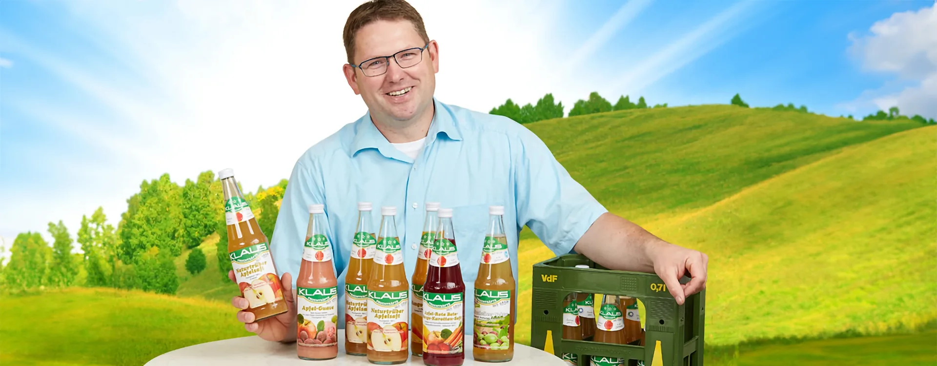 Mann steht an einem Tisch und präsentiert KLAUS Fruchtsäfte, im Hintergrund Wiesen und Hügel