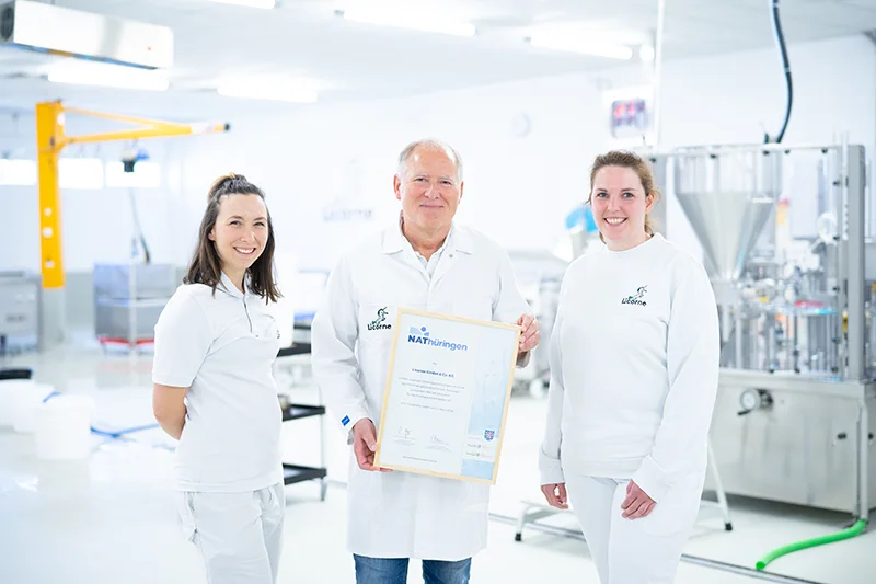 Claus Katzenberger und zwei Mitarbeiter von Licorne stehen im Werk und zeigen eine Urkunde