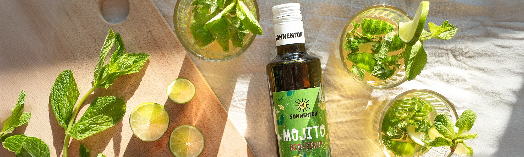 Virgin Mojito im Glas, Limette und Minze. Eine Flasche Mojito Sirup von Sonnentor.